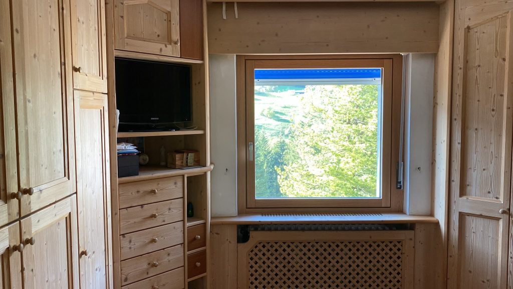 Finestra in legno in una baita di montagna in Trentino con vista sui prati