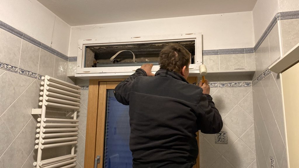 Posa delle finestre in un bagno: un posatore Antesi Serramenti lavora sul cassonetto durante la sostituzione